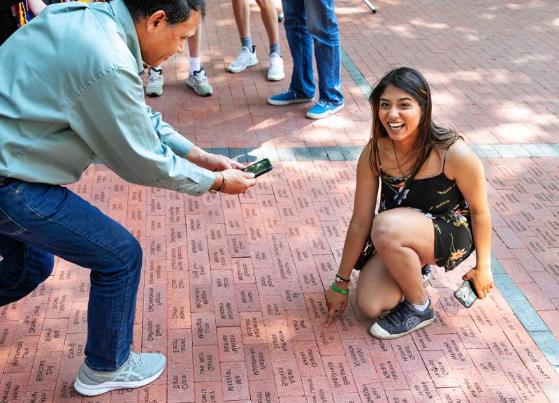 student points to a brick 那 has 的ir named engraved on a walkway